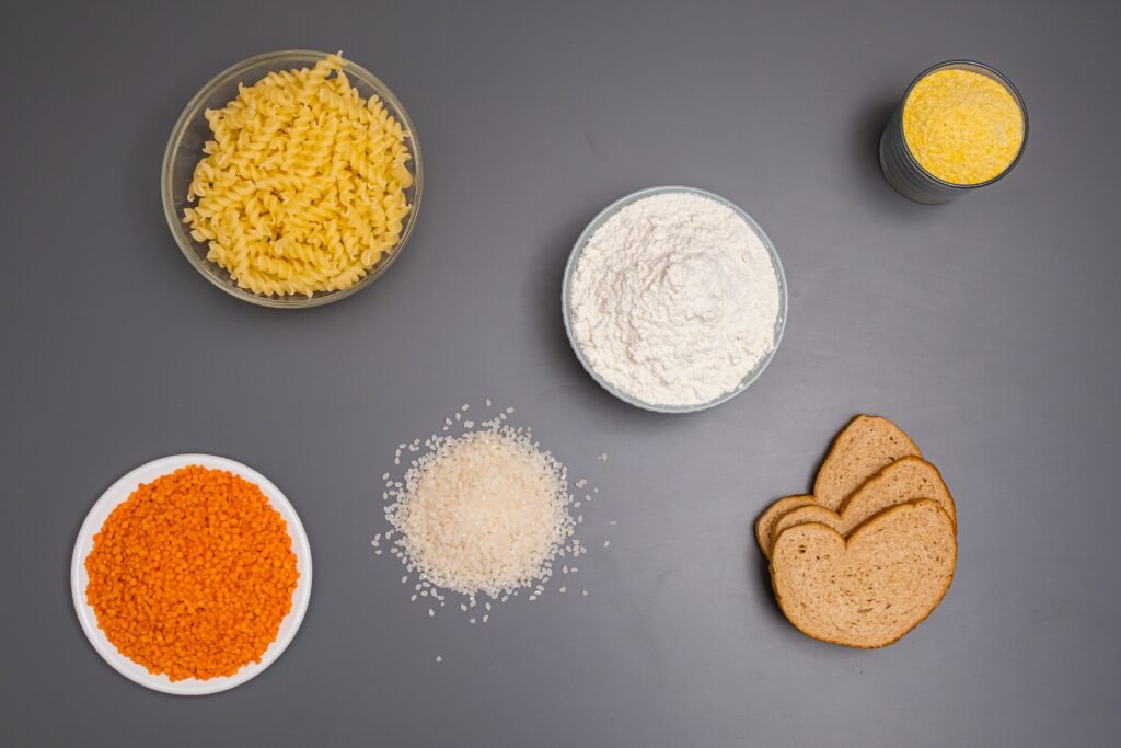 An assortment of dry ingredients including pasta, rice, and bread displayed on a grey background.