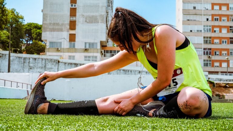 A young woman in a neon vest stretching on grass, preparing for an outdoor workout or running event.