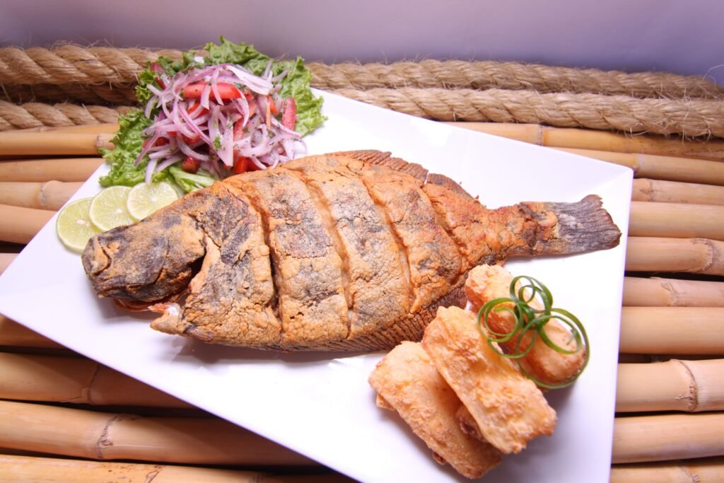 Delicious fried fish served with fresh vegetable salad and lime slices on a bamboo plate.
