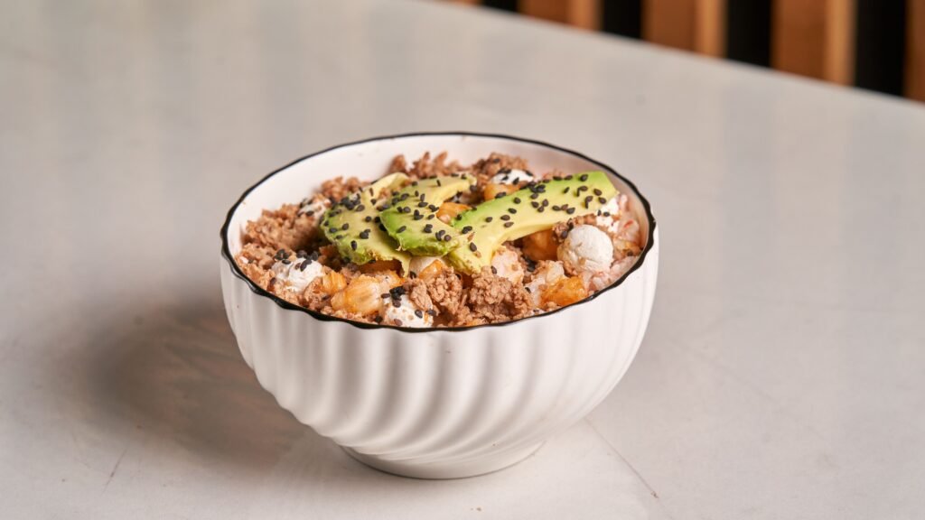 Healthy breakfast bowl featuring avocado, granola, and sesame seeds in a white dish.