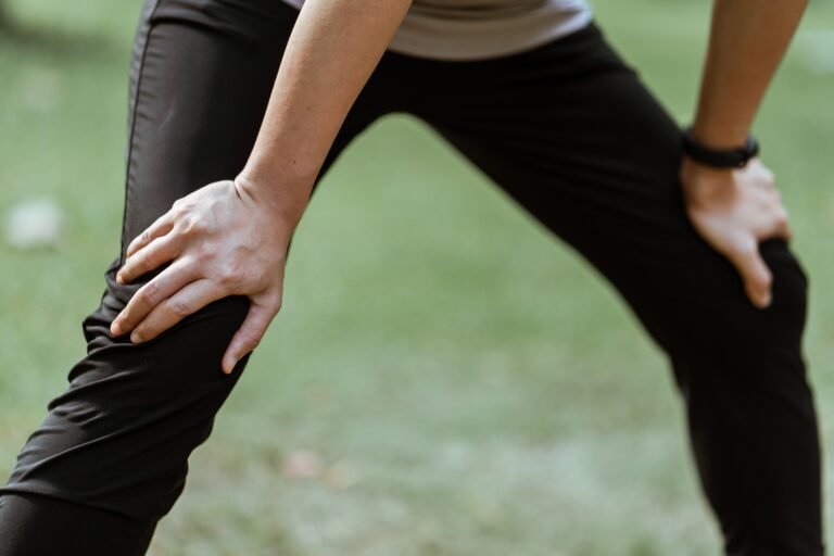 Crop unrecognizable sportsperson standing on recovery posture with hands on knees after active workout in green park