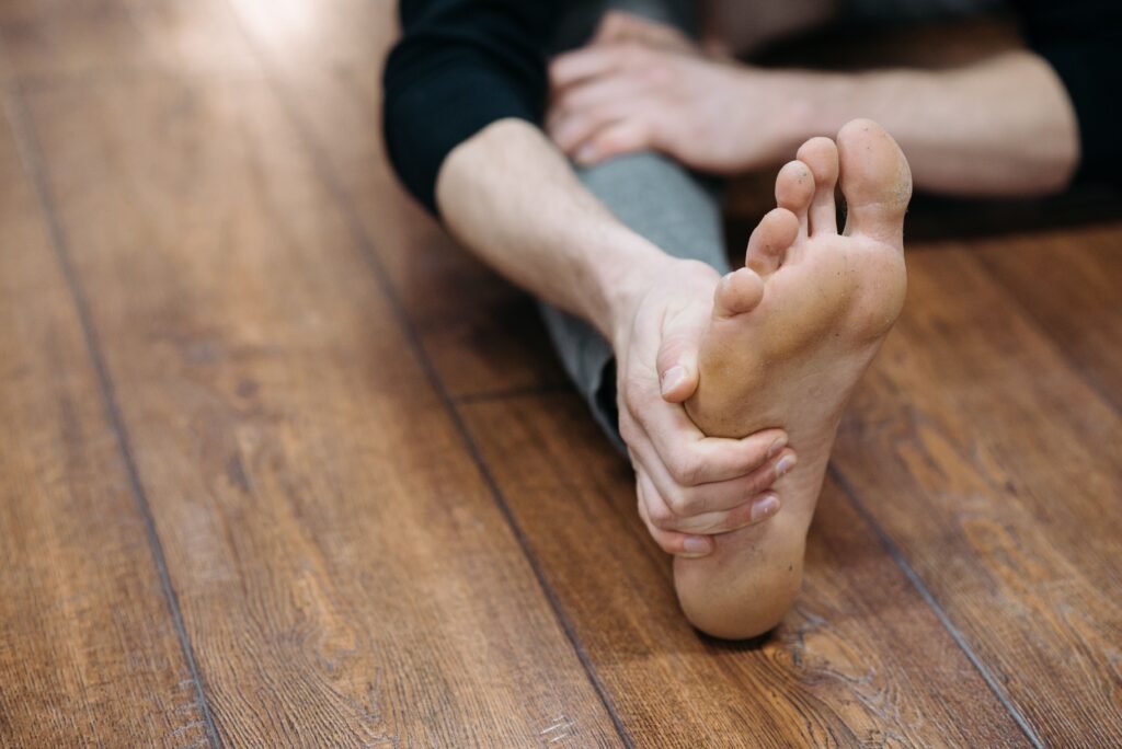 Close-up of a person doing a stretching exercise on a wooden floor, focusing on their bare foot.