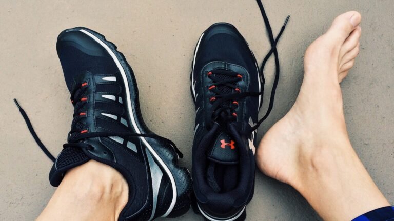 A pair of black sneakers next to bare feet on a gray surface.