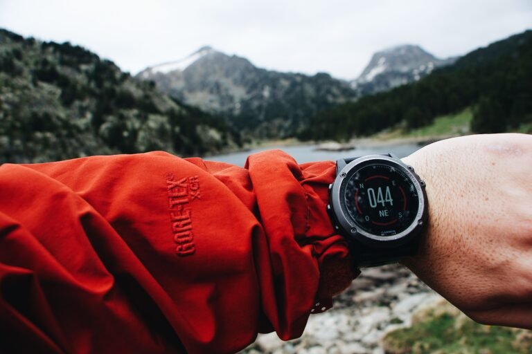 A hiker checks digital watch amid mountainous landscape. Adventure awaits.