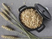 Flat lay of rolled oats in a black pot surrounded by wheat stalks on a textured surface.