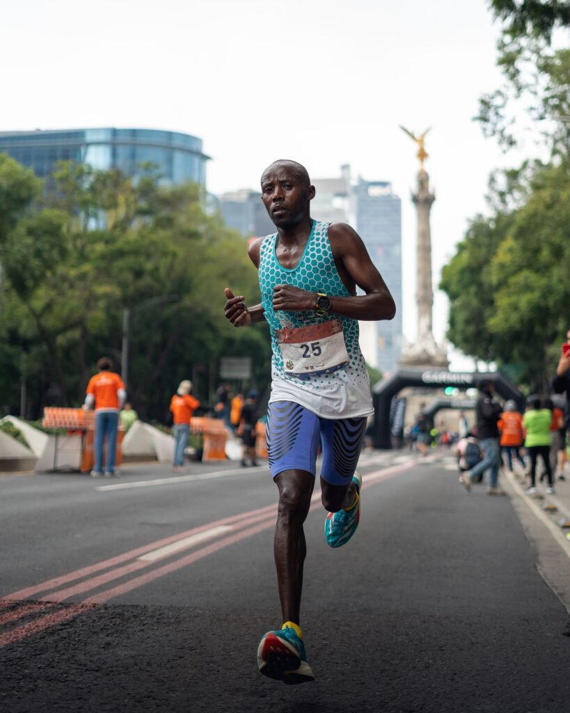 Focused runner participating in an urban marathon near a city landmark with support staff in the background.