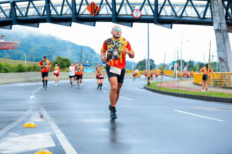 Marathon runner in colorful attire racing under a city overpass on a rainy day.