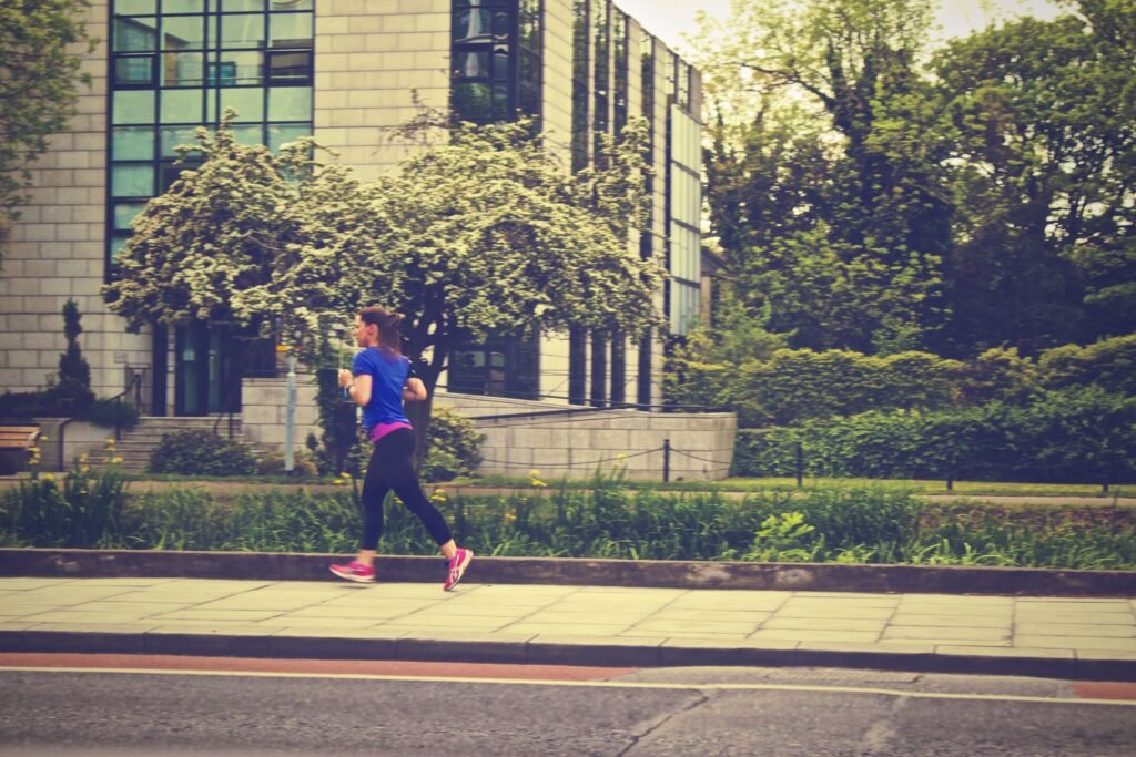 A woman running along a city street during the day surrounded by nature.